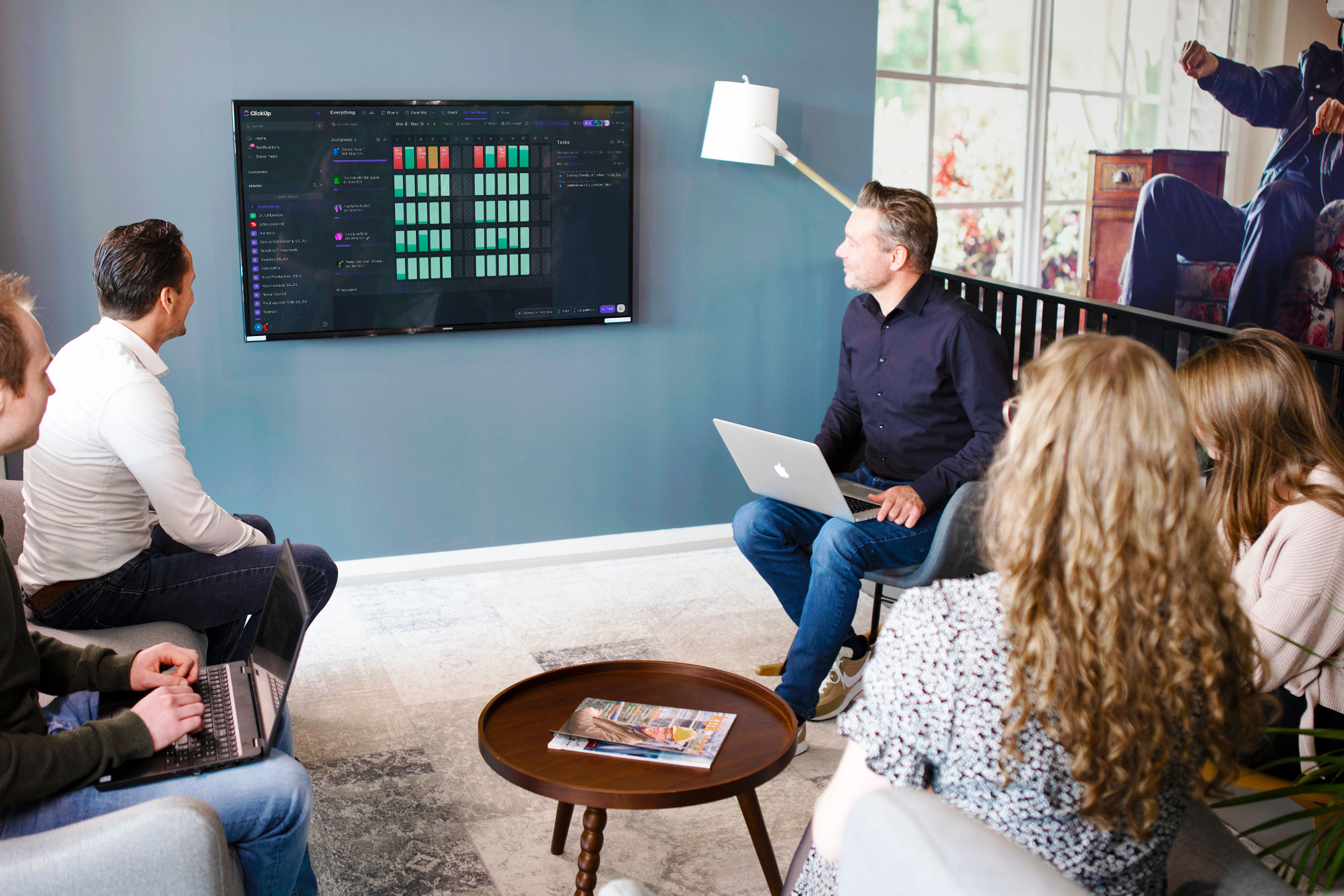 een groep mensen die in een kamer zitten met een televisie en een persoon die voor hen staat